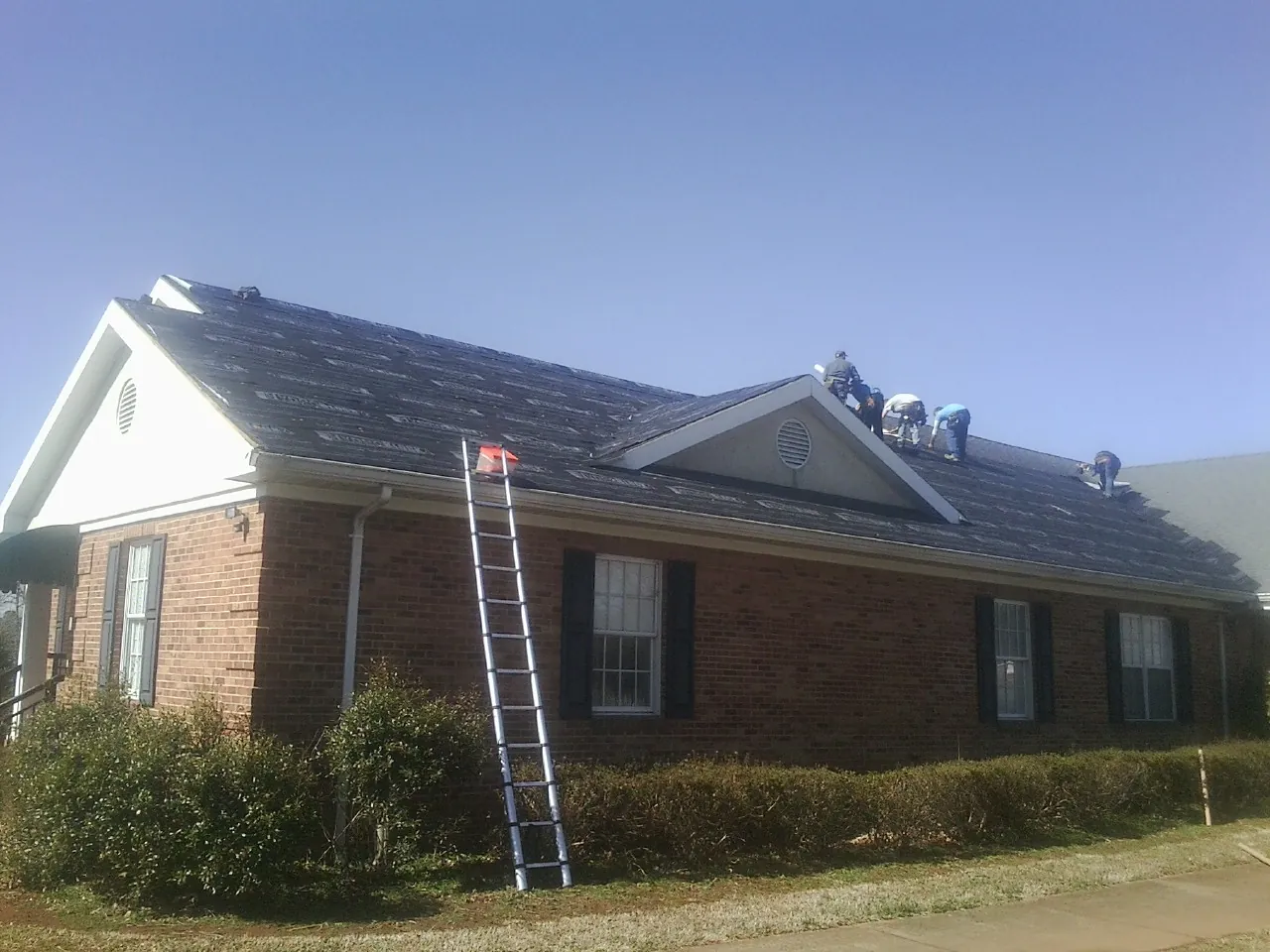 Crew tearing shingles off a brick ranch roof with a ladder set — Emergency Roof Repair work by our crew in Monterey