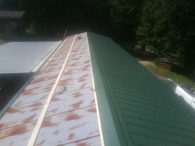 Old rusted panels beside newly installed green metal roofing — Wind Damage Roof Repair by Roofing Brothers in Monterey