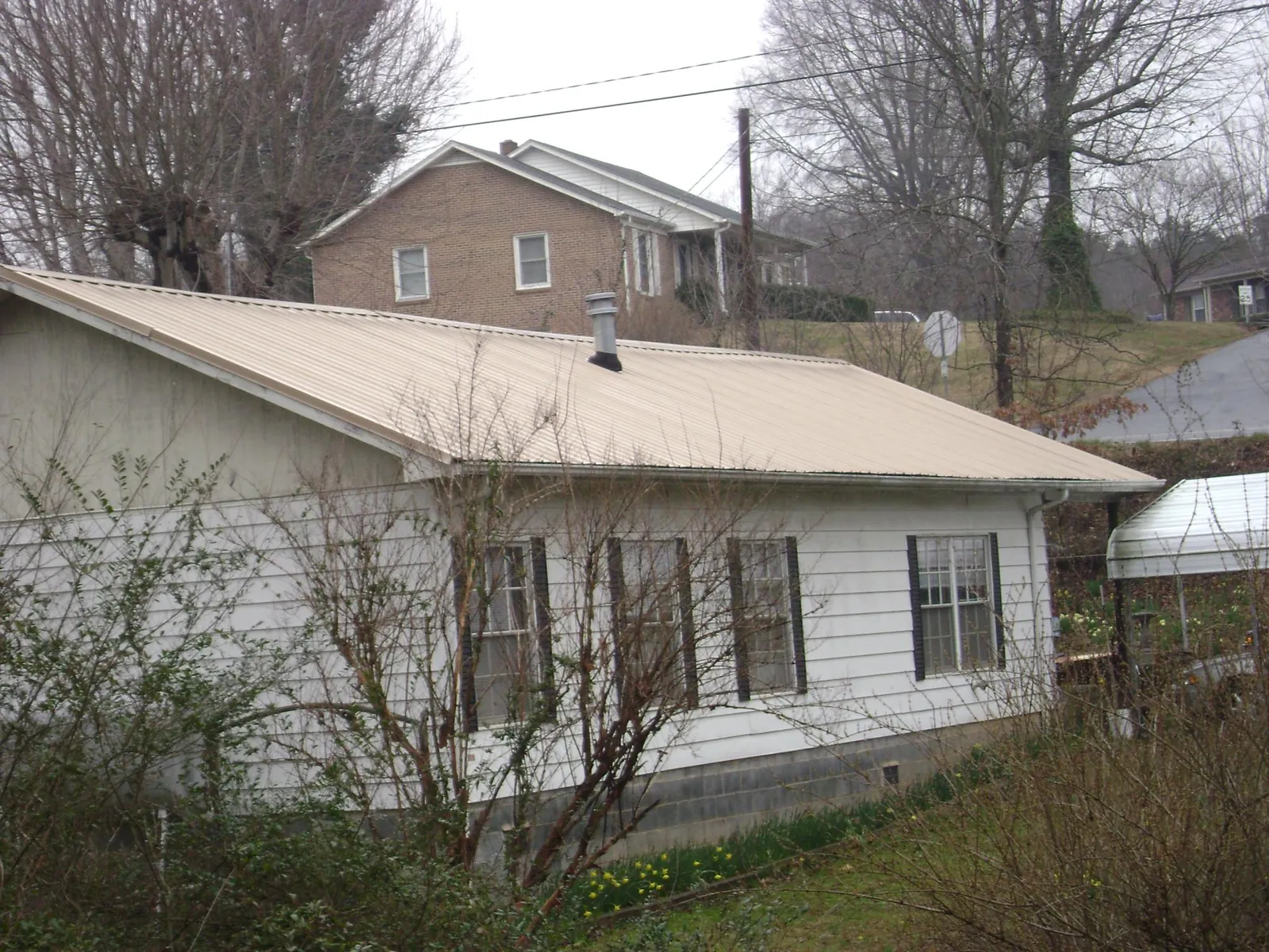 Tan metal roof on a white sided house set into a hillside — Commercial Roofing by Roofing Brothers in Monterey